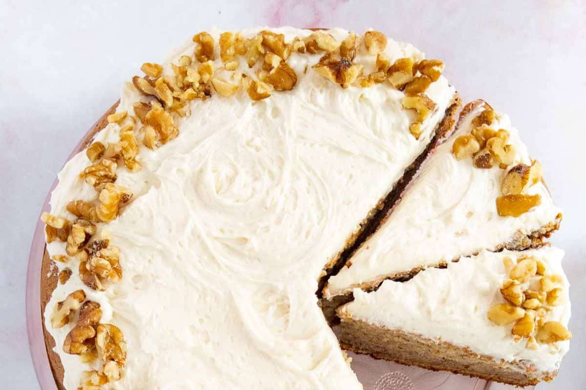 A frosted cake with walnuts on top, one slice partially removed, sits elegantly on a pink cake stand, offering a delightful gluten-free treat perfect for Easter desserts.