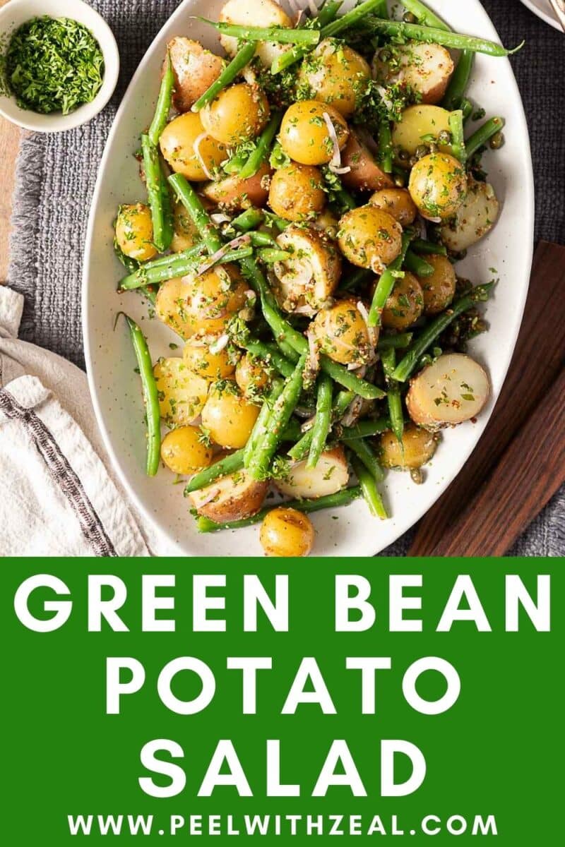 Oval platter with green bean potato salad, garnished with herbs, sits on a table alongside a napkin and a small bowl of chopped herbs.