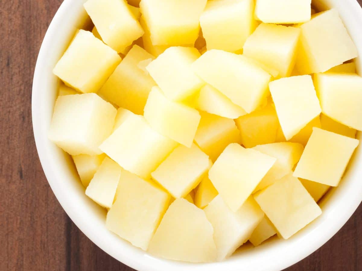A bowl filled with diced poatoes on a wooden surface.