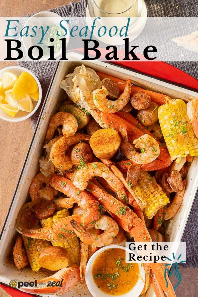 A seafood bake tray filled with cooked seafood, corn, potatoes, and sausage, garnished with herbs, sits next to a bowl of lemon wedges and a glass of white wine.