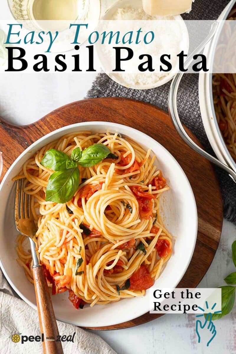 A bowl of Tomato Basil Pasta with fresh basil and rich tomato sauce, served with a fork; a pot and cheese sit in the background. Text reads “Easy Tomato Basil Pasta.”.