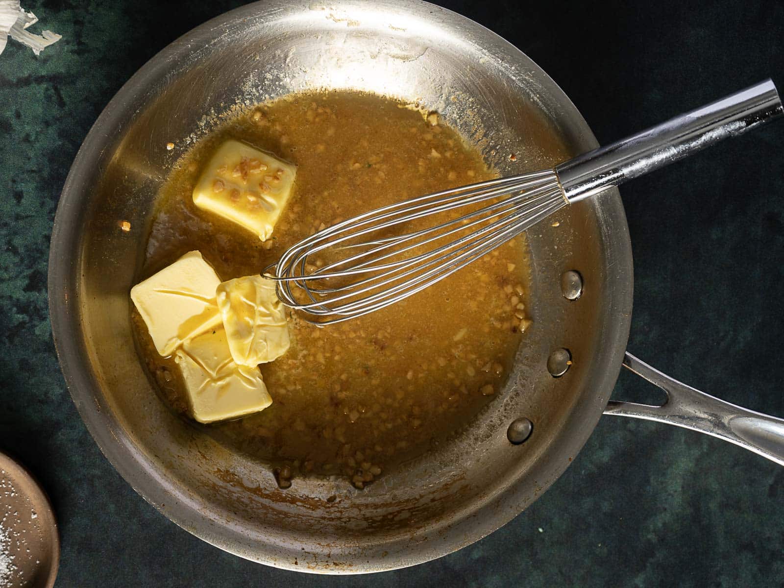A frying pan with melted butter and minced garlic being whisked into a brown sauce.
