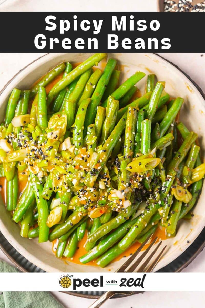 A bowl of miso green beans topped with scallions and sesame seeds, all coated in a spicy miso sauce, shown under the text "Spicy Miso Green Beans.