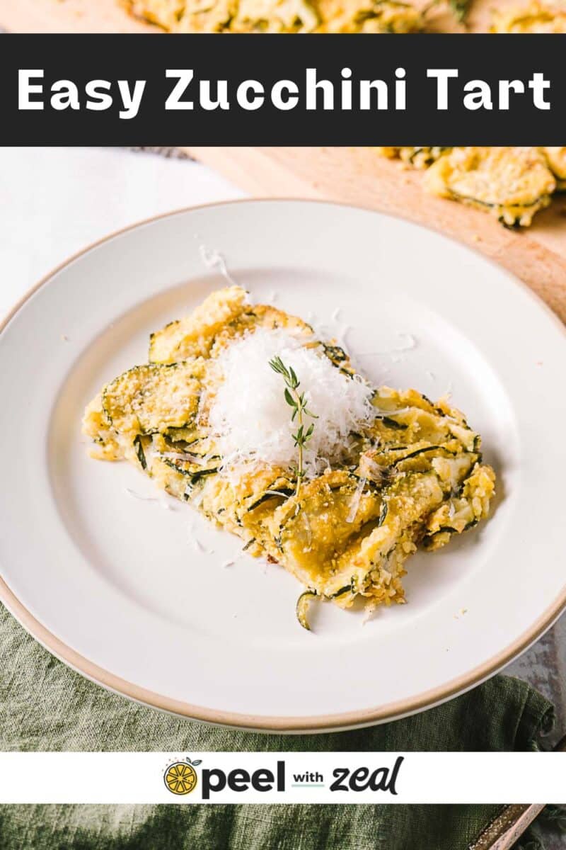 A slice of zucchini scarpaccia topped with grated cheese and a small herb sprig rests on a white plate. In the background, more pieces are elegantly arranged on a rustic wooden board, inviting you to savor this delightful Italian treat.