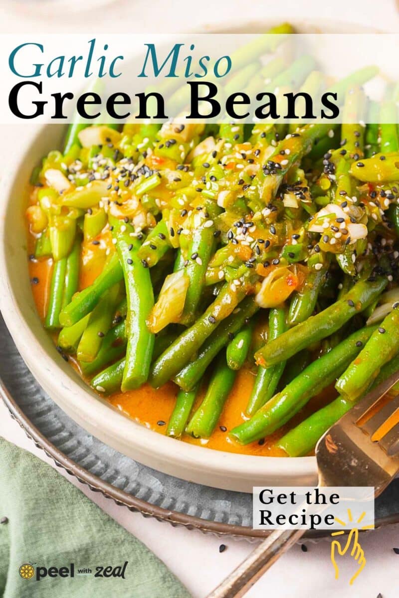 A bowl of miso green beans topped with garlic, miso sauce, and sesame seeds, garnished with chopped green onions.