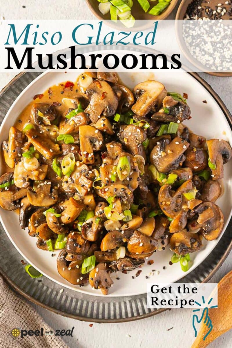 A plate of savory miso mushrooms glazed to perfection, garnished with chopped green onions and sesame seeds, with a fork and small bowl of sesame seeds nearby.