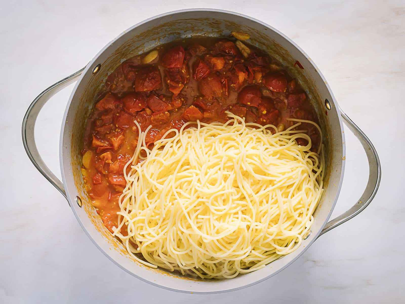 A pot of cooked spaghetti noodles and tomato-based sauce sits on a white surface, with noodles and sauce not yet mixed together.
