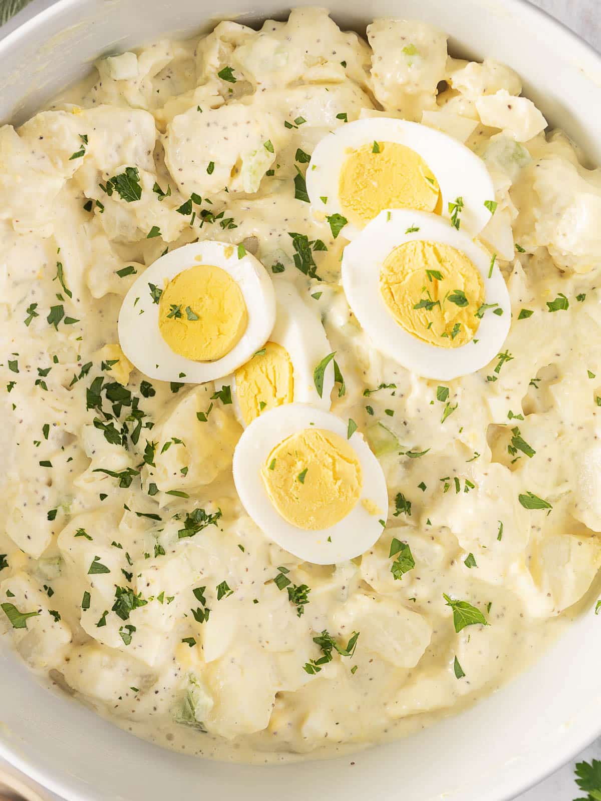 A bowl of potato salad topped with sliced hard-boiled eggs and sprinkled with chopped parsley.