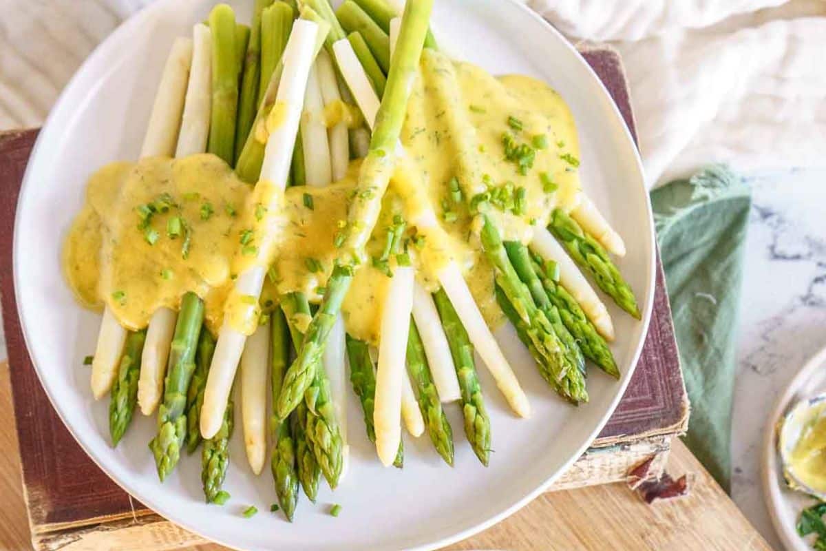 A plate of green and white asparagus topped with hollandaise sauce and garnished with chopped herbs, spotlighting a delightful gluten-free option for your Easter recipes.