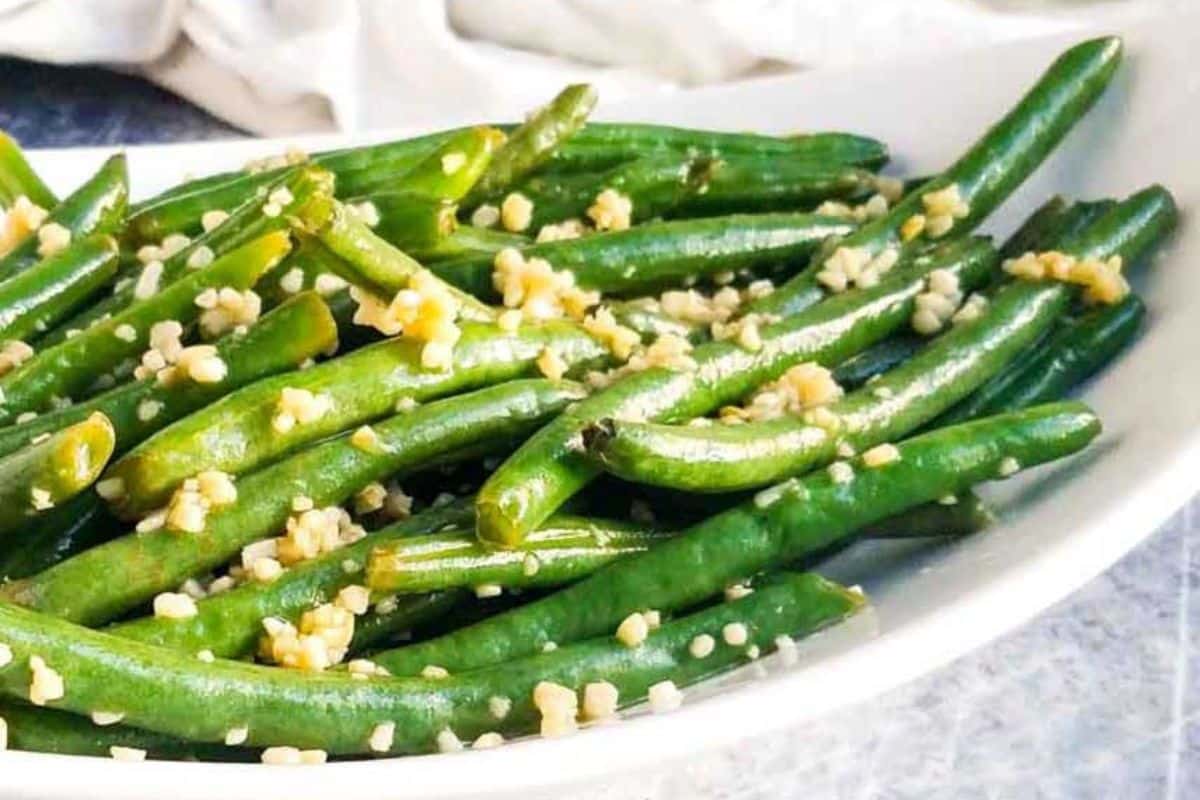 A plate of cooked green beans, a gluten-free delight, is topped with aromatic minced garlic.