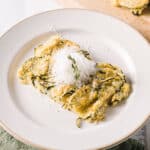 Plate of zucchini casserole topped with grated cheese and a sprig of thyme on a white plate.