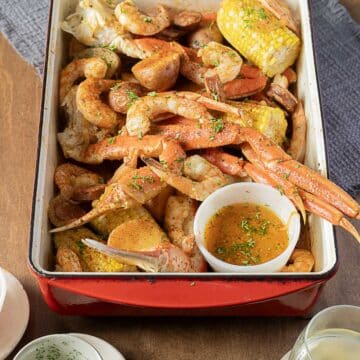 A tray of seafood boil with crab legs, shrimp, corn on the cob, potatoes, and a bowl of seasoned butter sauce on the side.