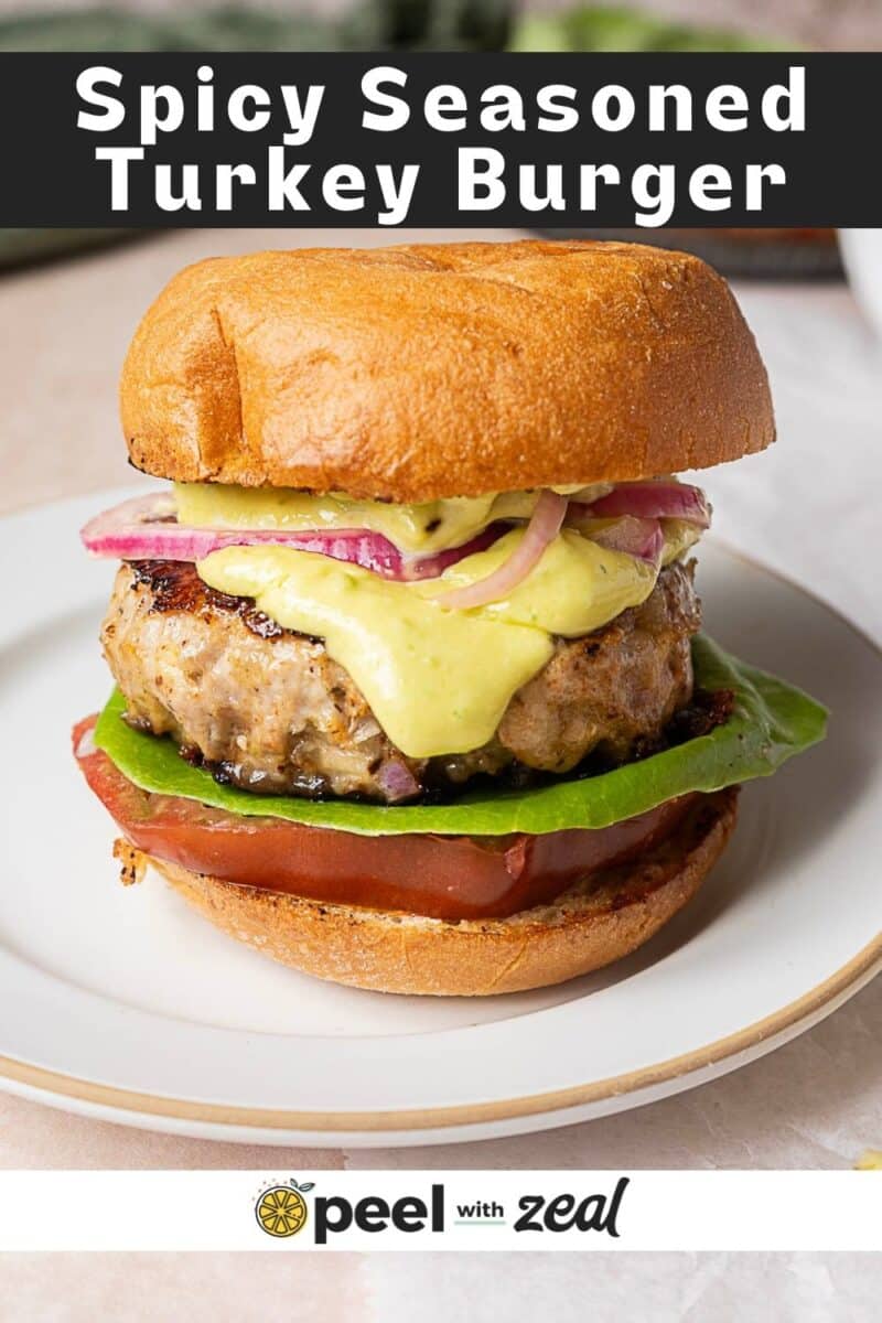 A turkey burger on a plate with tomato, lettuce, onions, and sauce in a toasted bun. Text reads "Spicy Seasoned Turkey Burger" and "peel with zeal." Try our spicy turkey burger recipes for an extra kick of flavor.