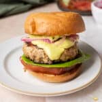 A turkey burger on a plate with lettuce, tomato, pickled onions, and yellow sauce in a toasted bun.