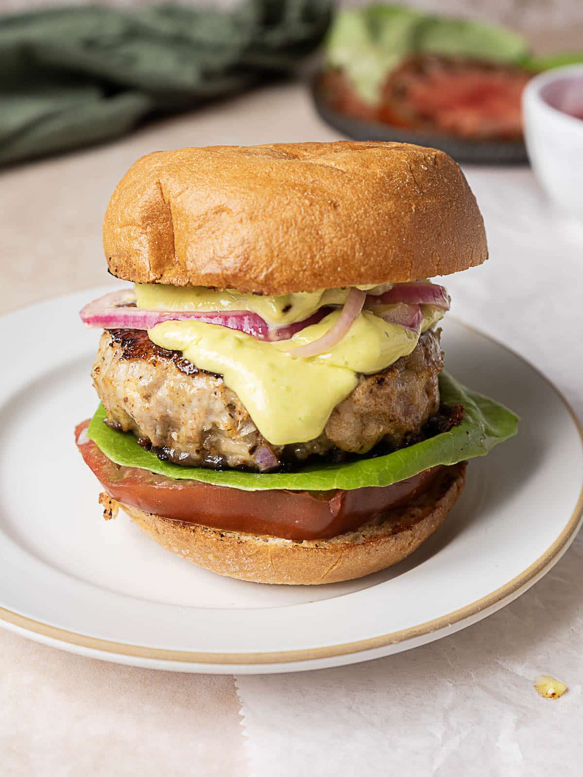 A turkey burger with lettuce, tomato, red onion, and yellow sauce in a toasted bun, served on a white plate.