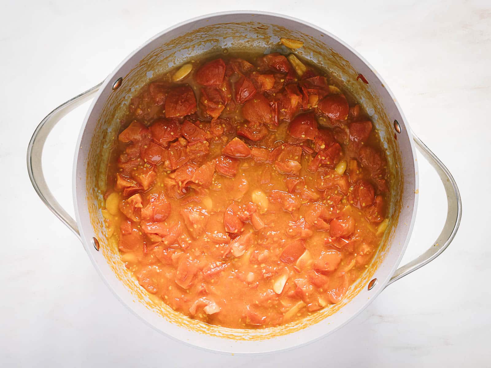 A pot filled with a simmering tomato sauce containing chunks of tomatoes and visible garlic cloves.