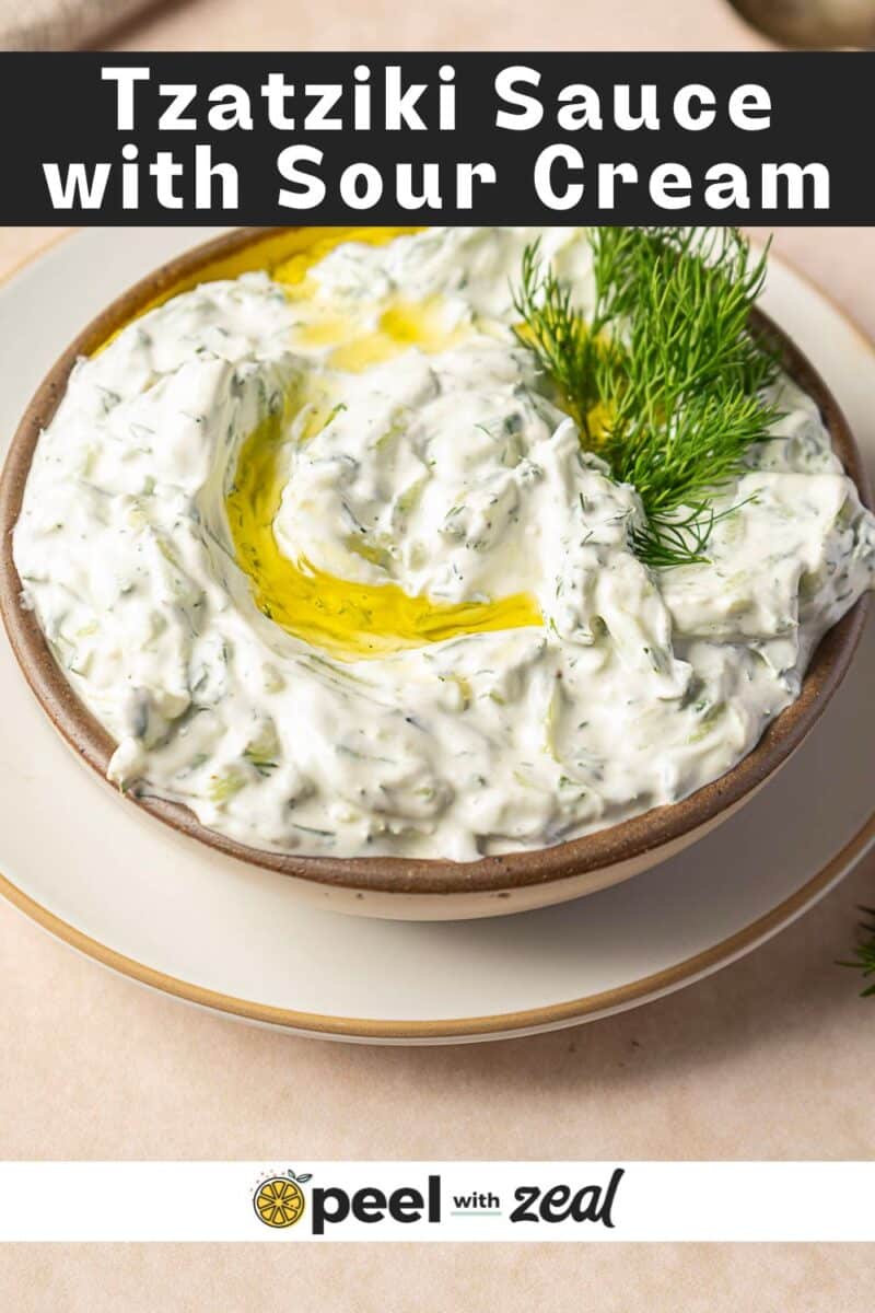 A bowl of Tzatziki Sauce with Sour Cream, garnished with olive oil and fresh dill, sits on a small plate. Text on the image reads, "Tzatziki Sauce with Sour Cream.