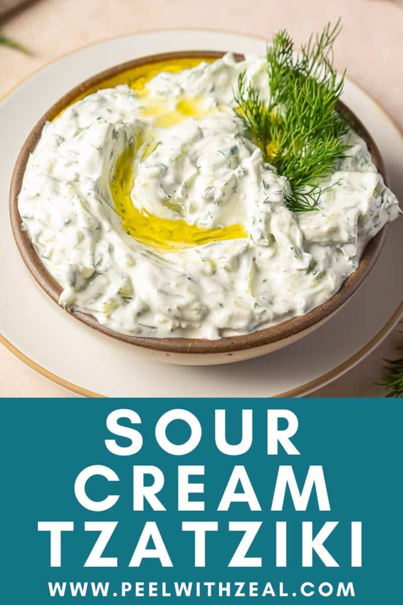 A bowl of Tzatziki Sauce with Sour Cream, garnished with olive oil and fresh dill, sits on a plate