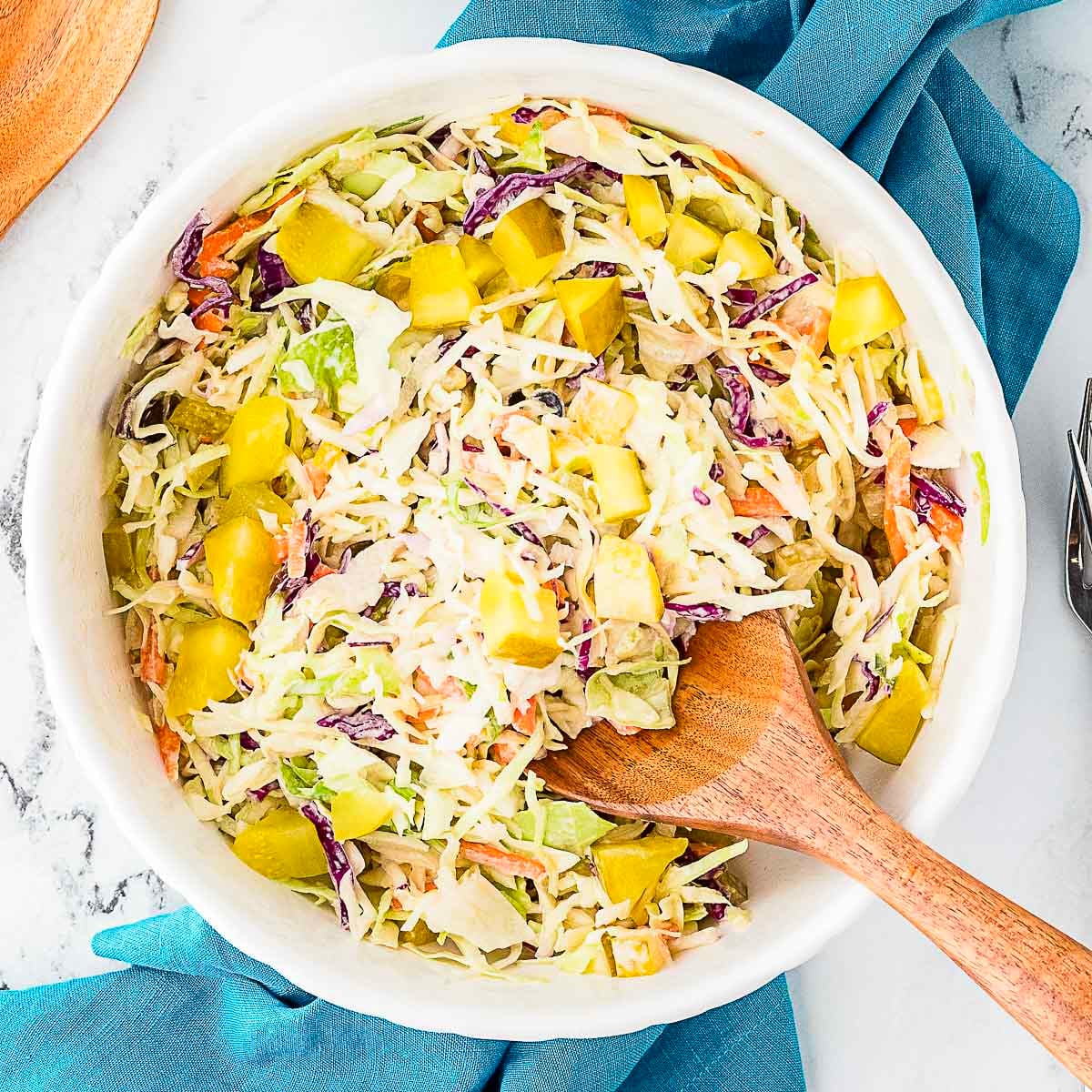 dill pickle coleslaw in a white bowl with a wooden serving spoon on the side