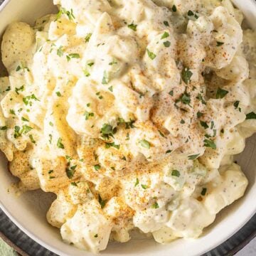 Bowl of creamy old fashioned potato salad topped with chopped herbs and a sprinkle of paprika.