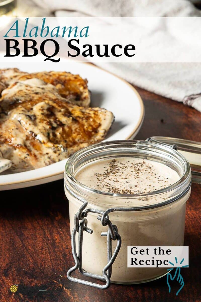 Glass jar of creamy Alabama white sauce on a wooden table, with grilled chicken on a plate in the background. Text overlay reads "Alabama BBQ Sauce" and "Get the Recipe.