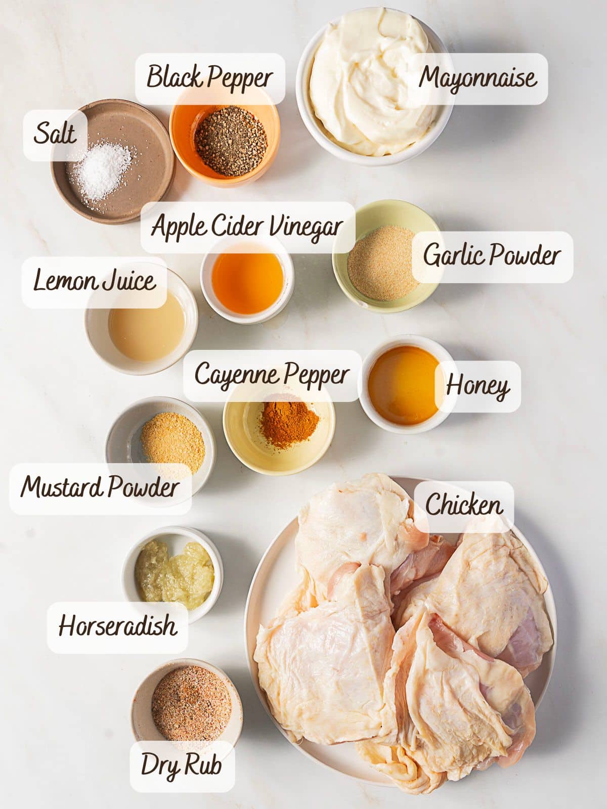 Ingredients for an Alabama chicken recipe laid out in bowls and plates, including chicken, mayonnaise, vinegar, seasonings, honey, horseradish, and lemon juice, all clearly labeled.