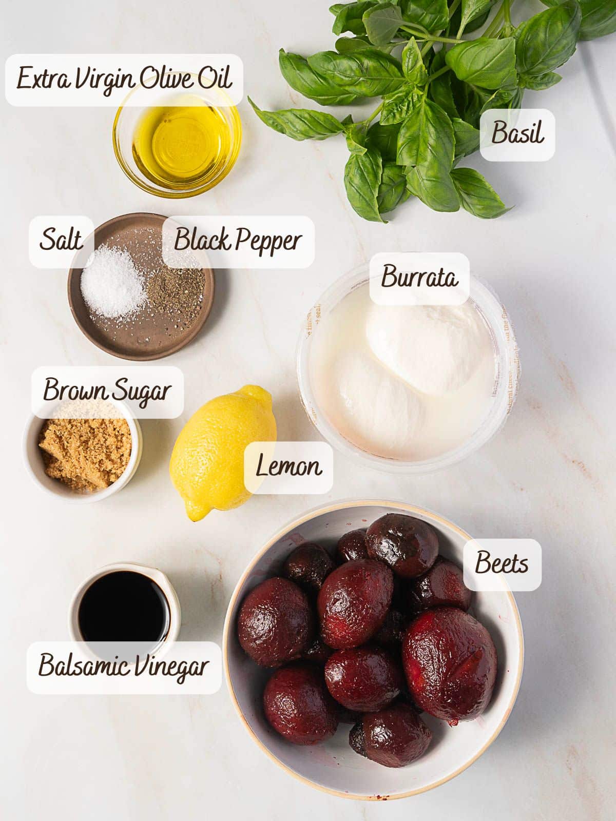 A selection of ingredients on a counter for a beet and burrata salad: extra virgin olive oil, basil, burrata, beets, lemon, balsamic vinegar, brown sugar, salt, and black pepper.