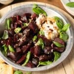A metal dish with roasted beet cubes, fresh basil leaves, a dollop of burrata cheese, lemon zest, and a drizzle of balsamic glaze.