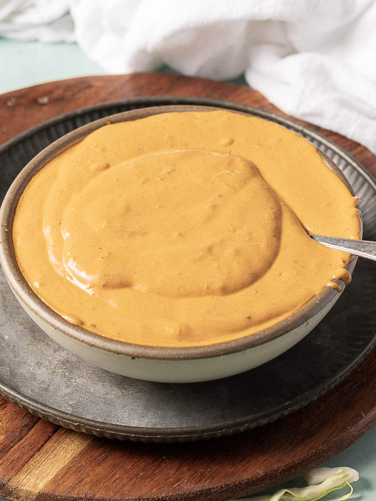 A bowl filled with smooth, light brown sauce placed on a metal tray with a spoon inside the bowl.
