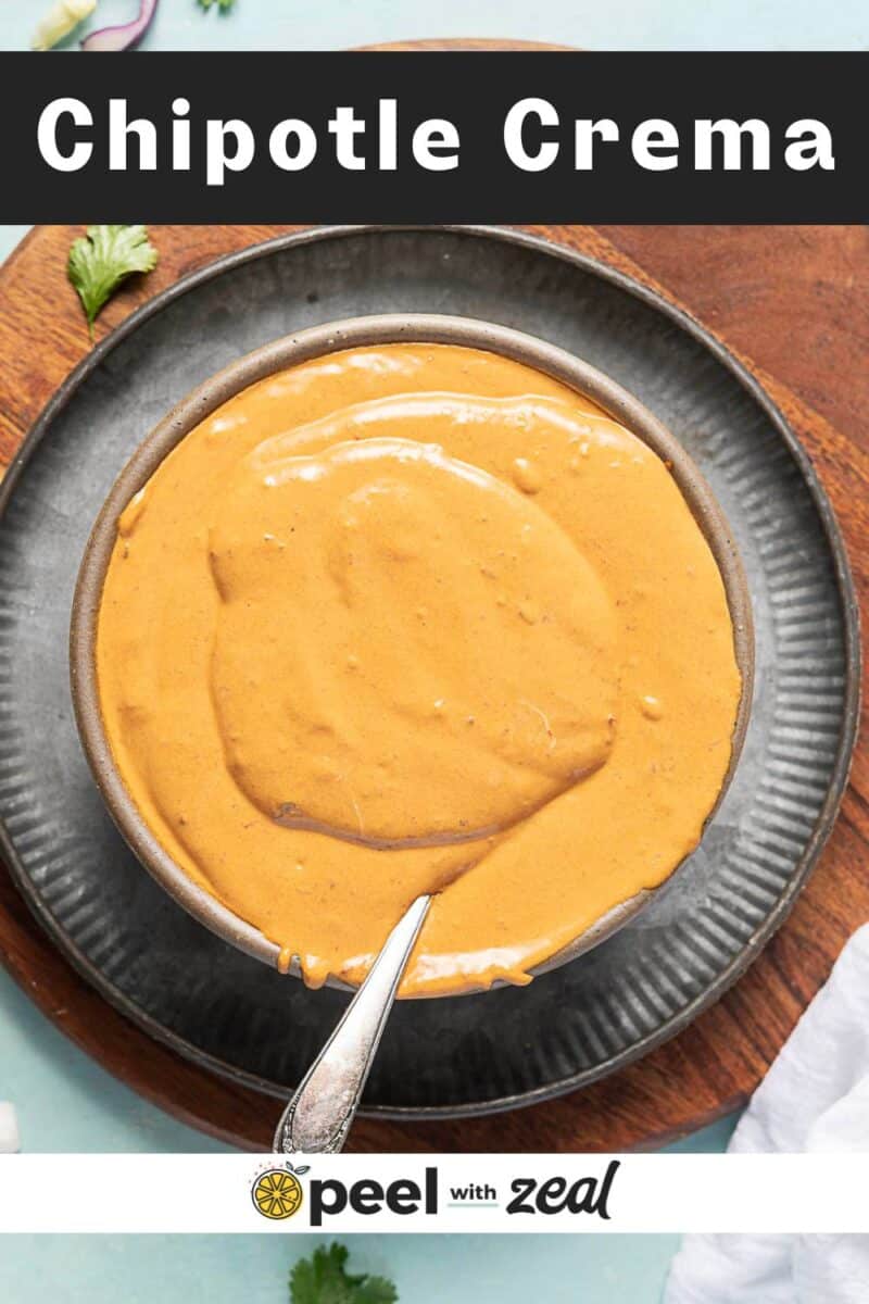 A bowl of creamy orange chipotle crema made with chipotle sauce sits with a spoon on a dark plate atop a wooden board. Text reads "Chipotle Crema" at top and "peel with zeal" at bottom.