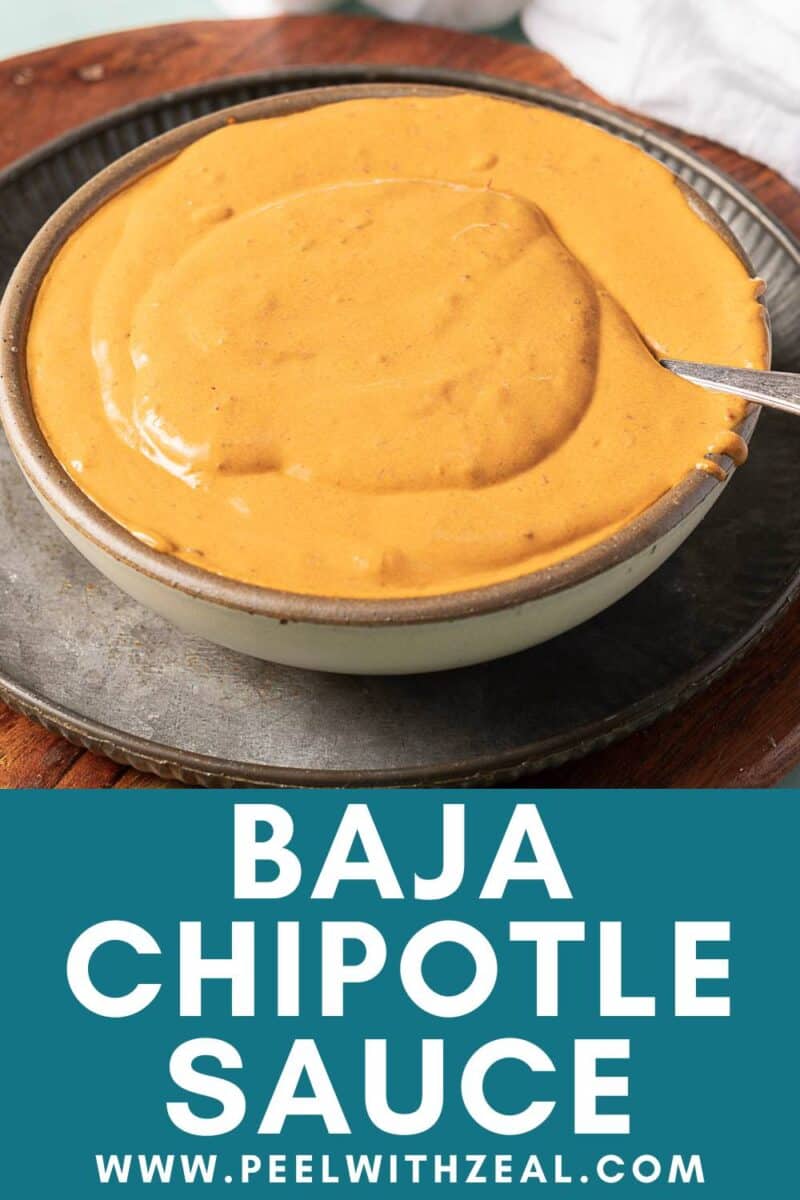A bowl of creamy orange chipotle sauce with a spoon, set on a plate.