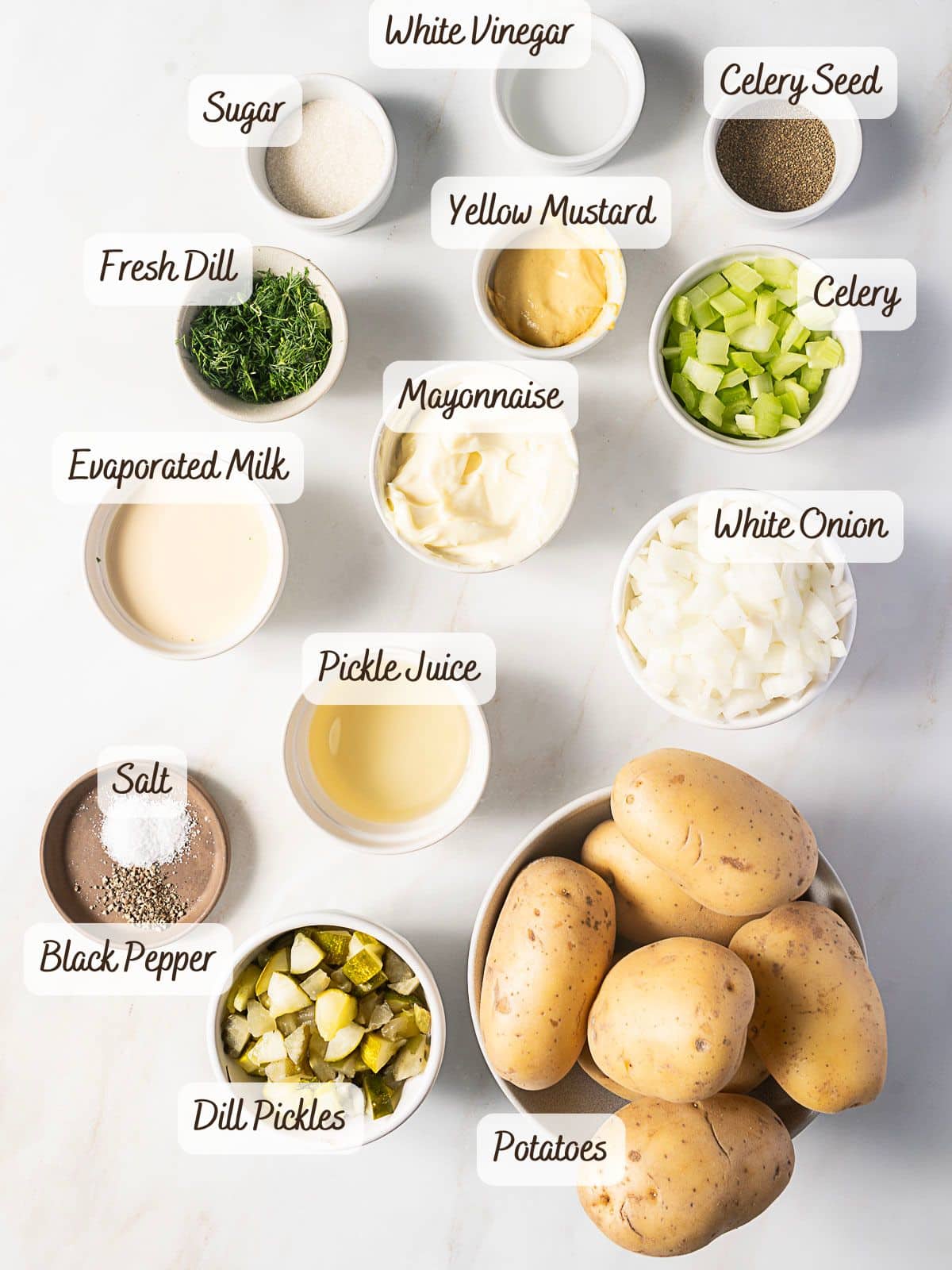 Top-down view of ingredients for potato salad with dill pickles, including potatoes, mayonnaise, celery, white onion, fresh dill, celery seed, salt, black pepper, sugar, white vinegar, and yellow mustard.