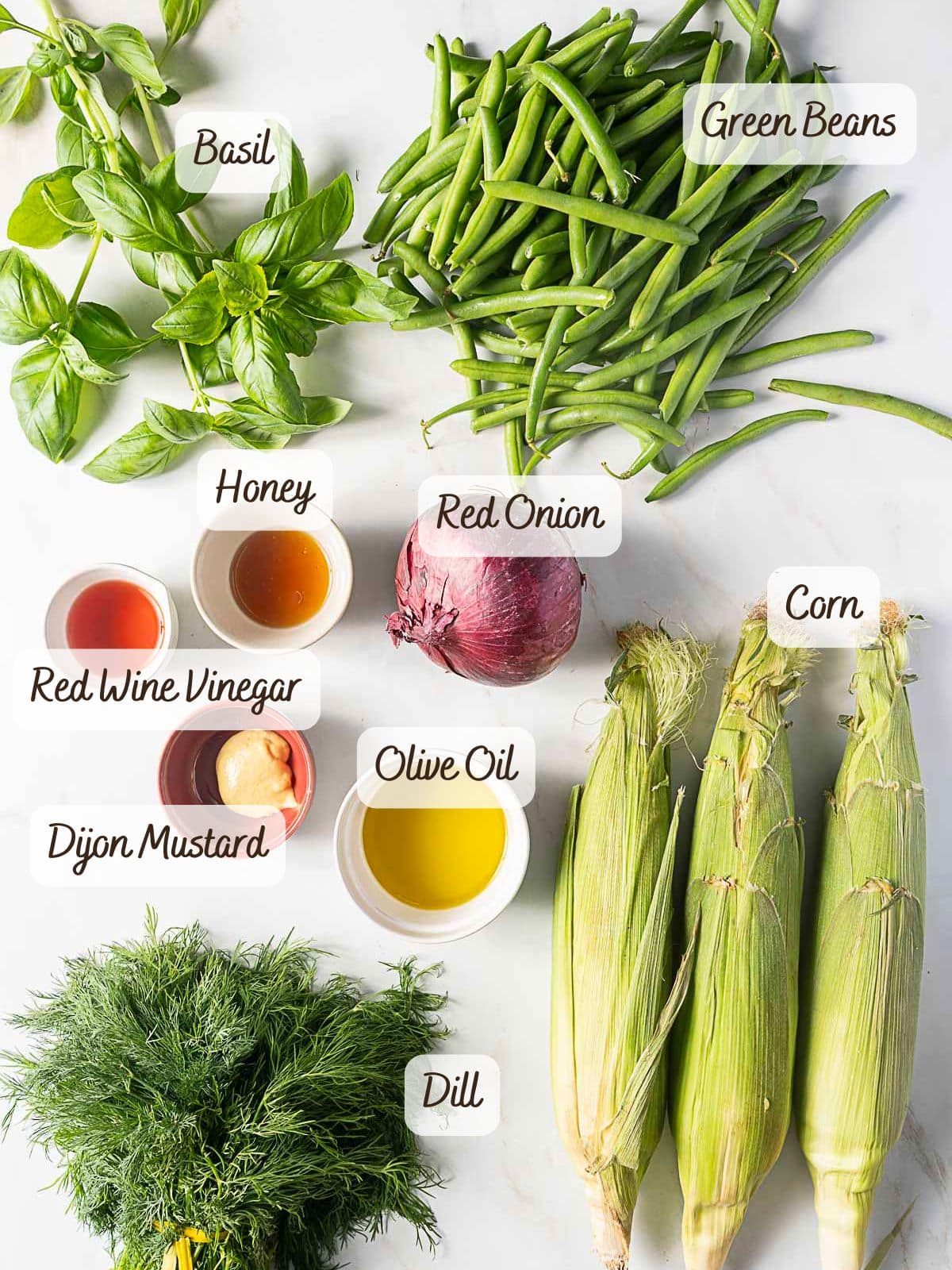 Fresh basil, crisp green beans, red onion, corn, and dill sit alongside small bowls of honey, red wine vinegar, Dijon mustard, and olive oil—perfect for crafting a vibrant green bean corn salad.