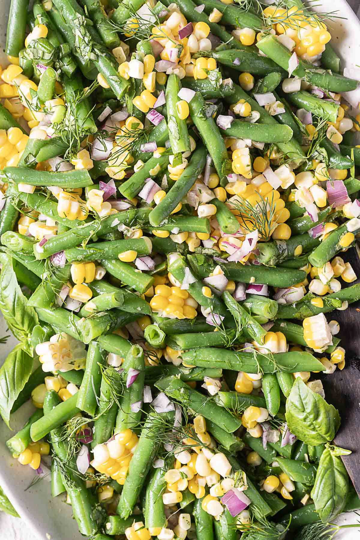 A salad made with green beans, corn kernels, red onion, and fresh herbs, arranged on a white plate.