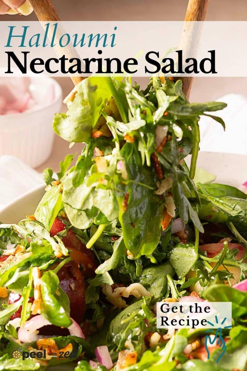 A close-up of a fresh nectarine salad with halloumi, arugula, onions, and a light dressing, served in a white bowl with wooden utensils.