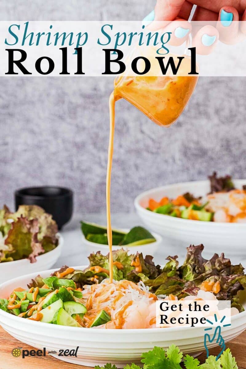 A hand pours sauce over a bowl filled with shrimp, rice noodles, lettuce, cucumbers, carrots, and herbs. Two similar bowls are visible in the background.