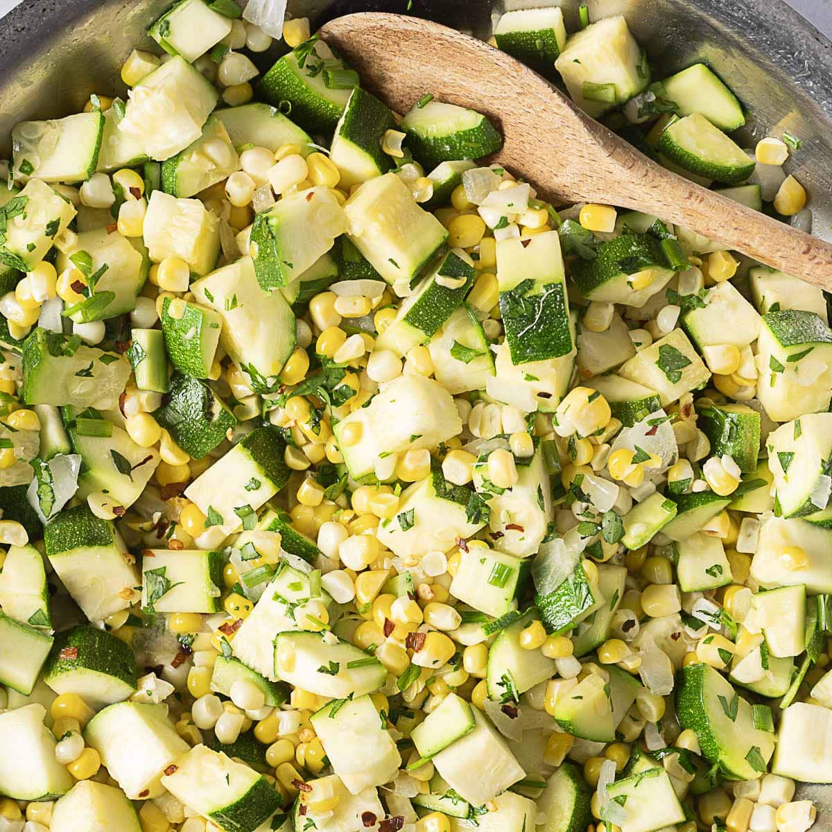 sauteed zucchini and corn in a stainless bowl with a wooden spoon on the side