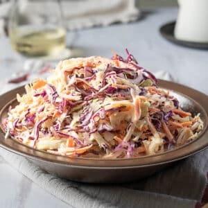 A plate of coleslaw made with shredded red and green cabbage, carrots, and creamy dressing sits on a table.