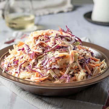 A plate of coleslaw made with shredded red and green cabbage, carrots, and creamy dressing sits on a table.