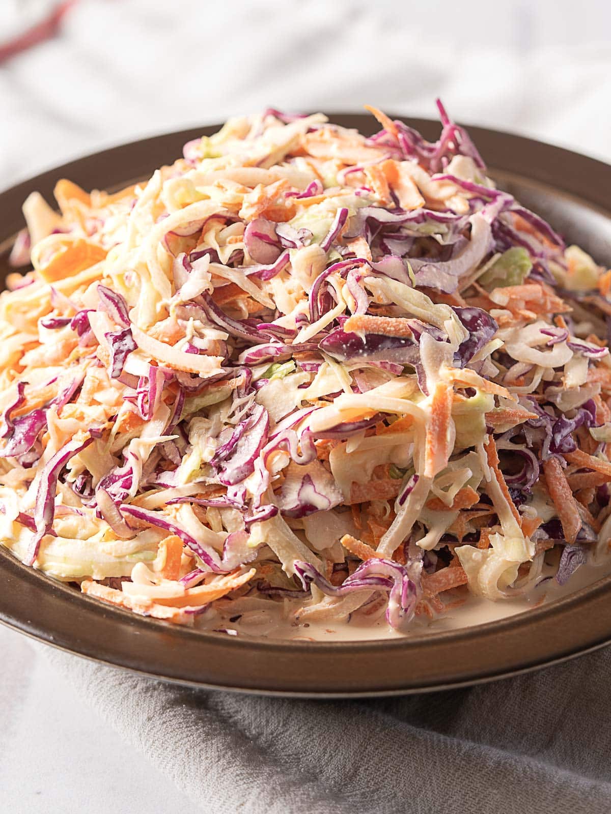 A plate of coleslaw made with shredded green and purple cabbage, carrots, and creamy dressing.