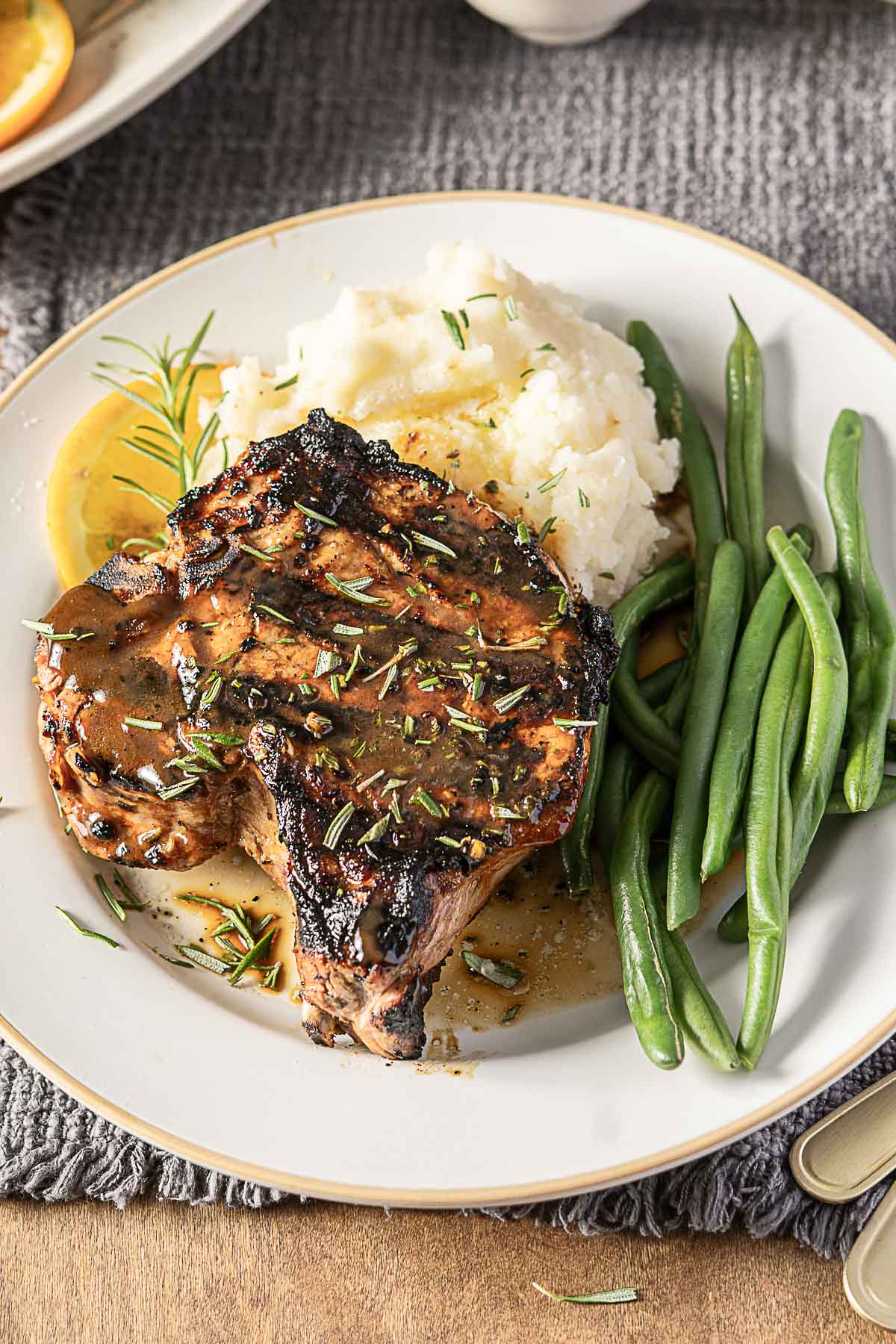 Grilled pork chop with sauce, served with mashed potatoes and green beans on a white plate.