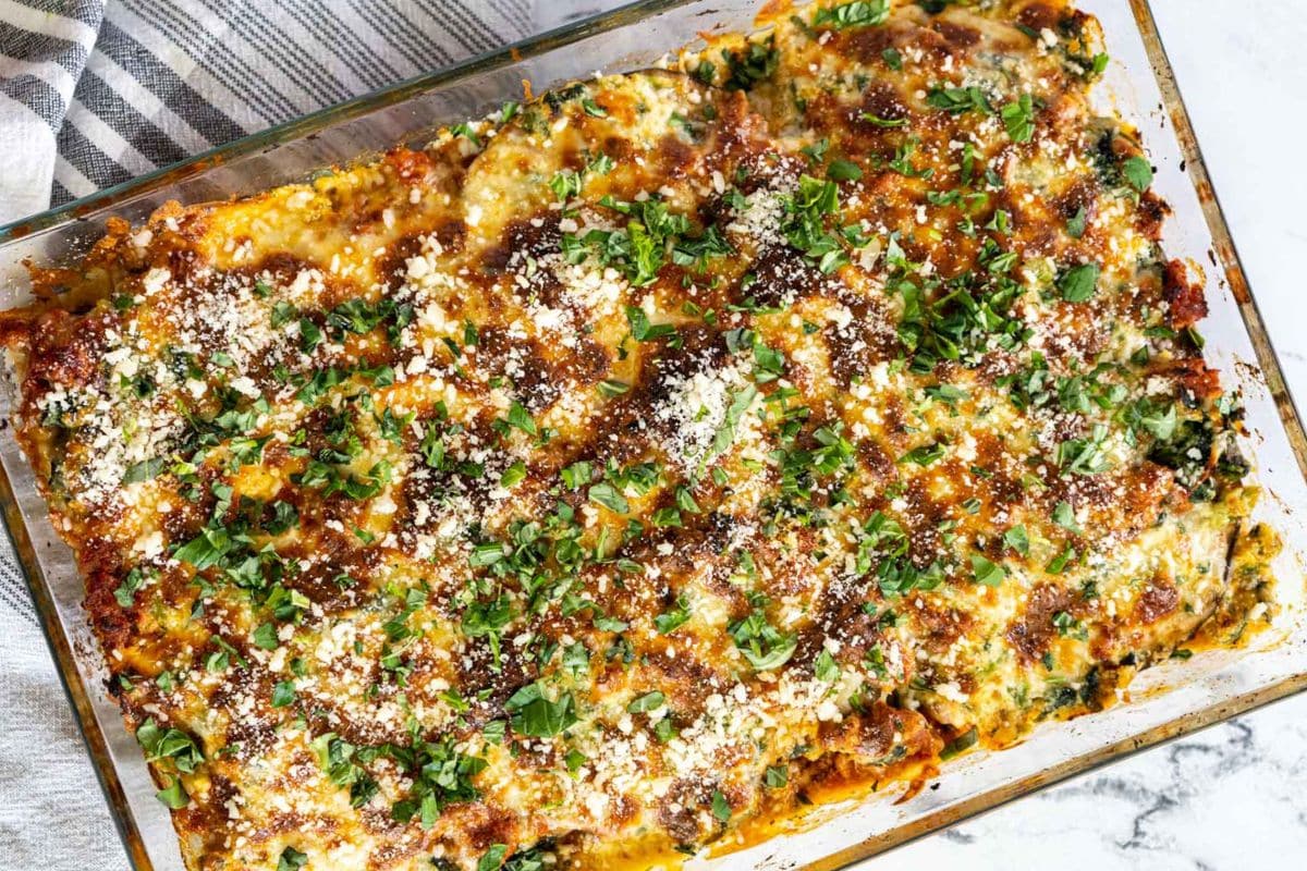 A baked casserole dish filled with lasagna and tender eggplant, topped with melted cheese, tomato sauce, herbs, and a sprinkle of chopped fresh parsley-perfect for fans of comforting eggplant recipes.