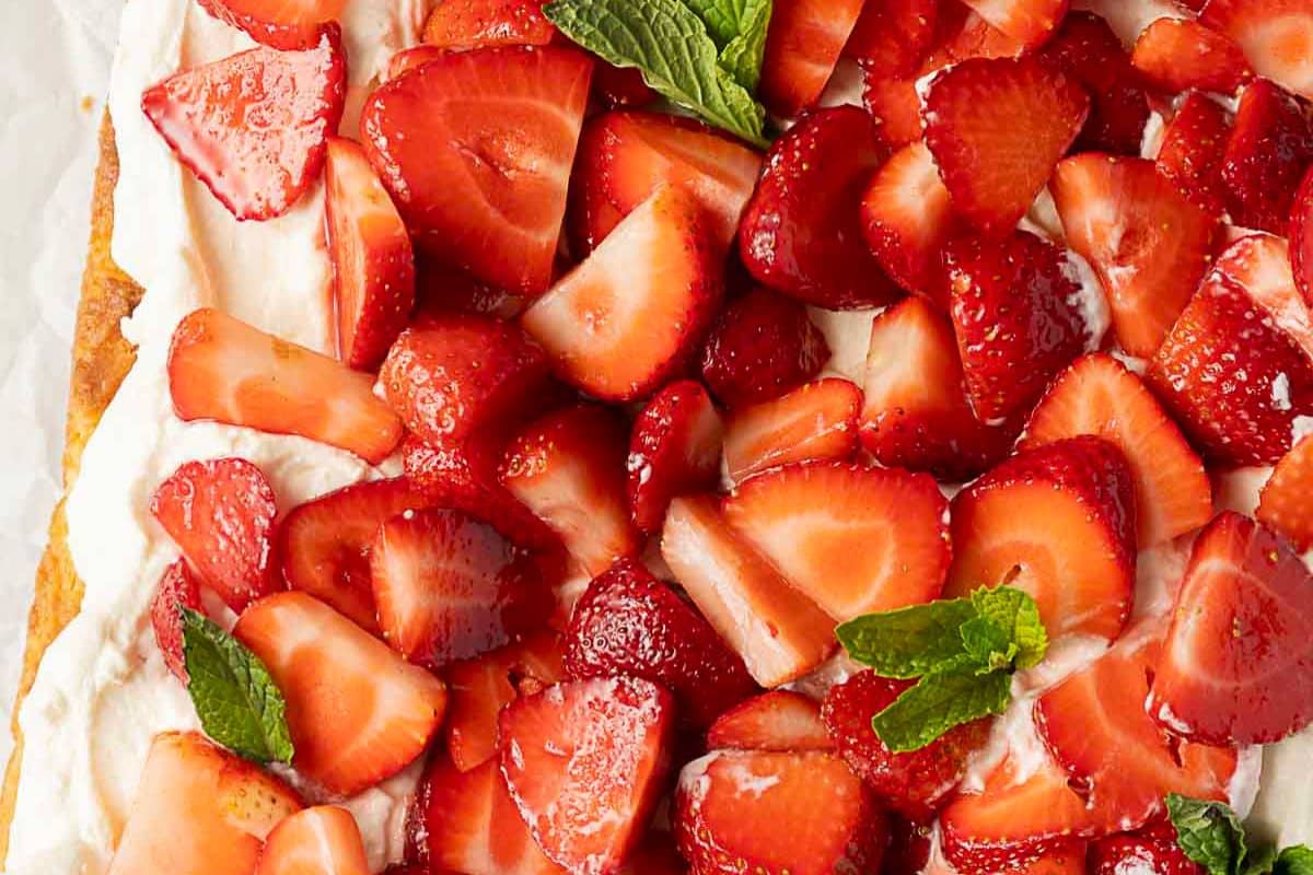 Close-up of sliced strawberries on a layer of whipped cream, garnished with fresh mint leaves.