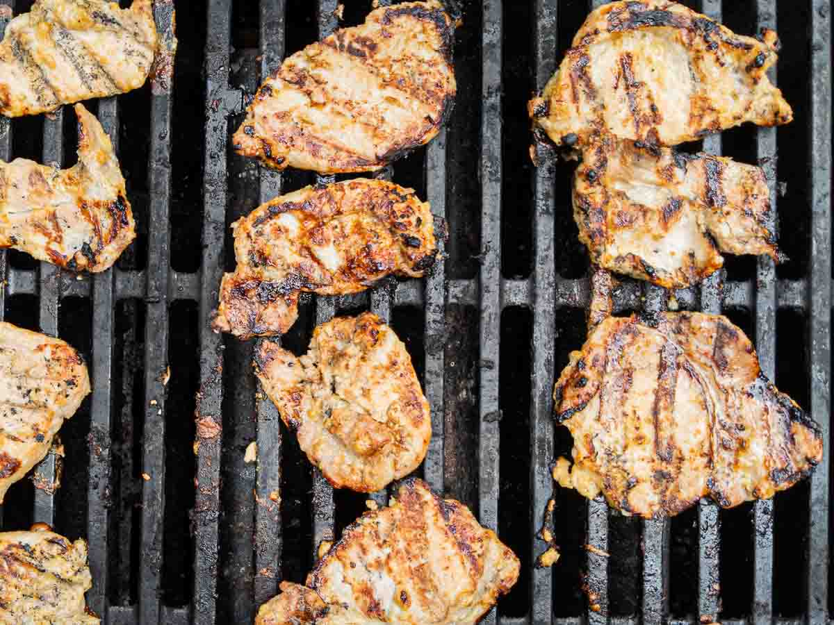 Several pieces of grilled meat are cooking on a barbecue grill, showing distinct grill marks and a slightly charred surface.