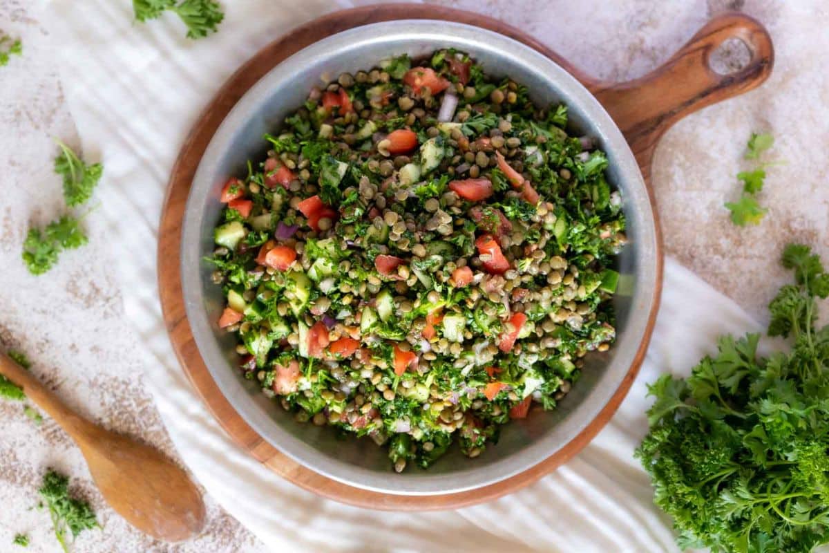A bowl of lentil salad with chopped ripe tomatoes, parsley, and vegetables on a wooden board, with a wooden spoon and fresh parsley nearby-one of the must-try tomato recipes for any fresh meal.