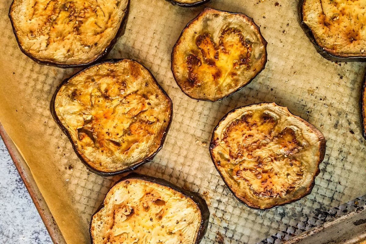 Slices of roasted eggplant on a parchment-lined baking sheet, lightly browned and seasoned-a simple favorite among eggplant recipes and a delicious way to cook eggplant.