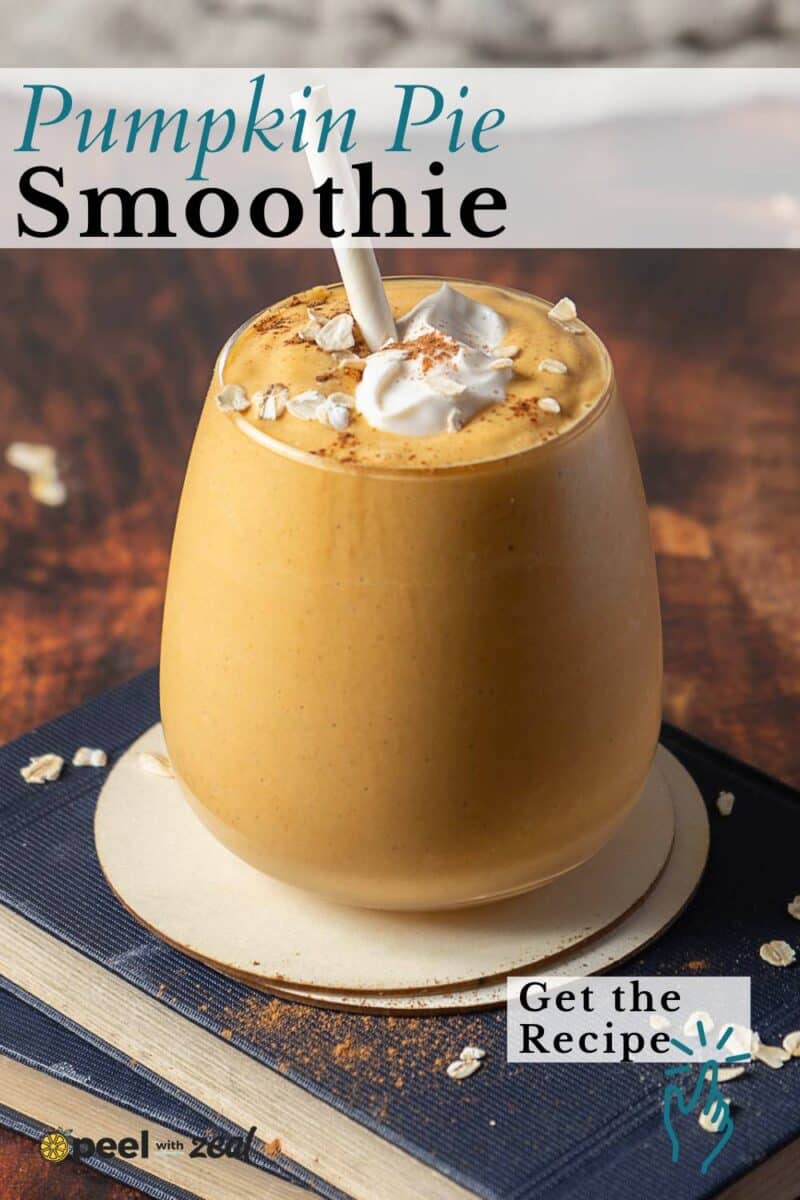 A glass of pumpkin smoothie topped with whipped cream, oats, and cinnamon, with a straw, sits invitingly on a stack of books.