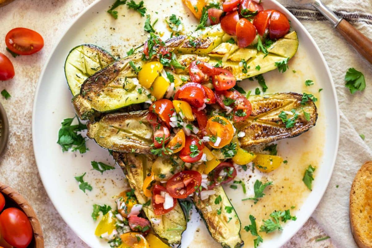A plate of roasted zucchini halves topped with a vibrant salsa of ripe tomatoes, onion, and herbs, garnished with chopped parsley—the perfect summer dish for fans of fresh tomato recipes.