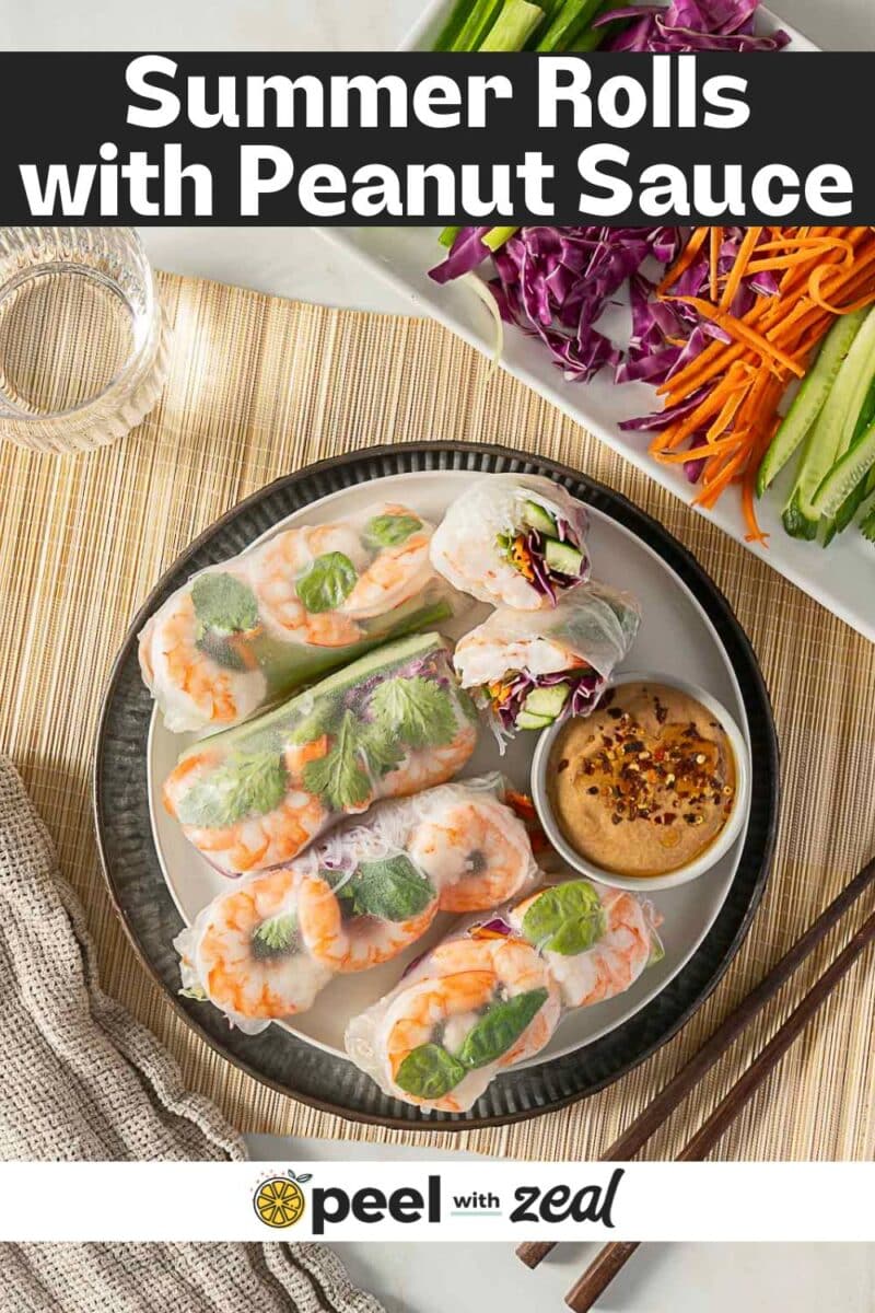 A plate of shrimp summer rolls with vegetables and fresh herbs, served with peanut sauce; glass of water and sliced veggies on the side. Text overlay reads “Shrimp Summer Rolls with Peanut Sauce.”.