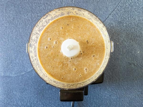Overhead view of a food processor containing a blended brown liquid mixture, sitting on a dark textured surface.